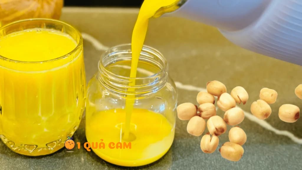 Rót sữa bí đỏ hạt sen vàng óng từ máy xay vào hũ thuỷ tinh, bên cạnh là ly sữa đã rót và vài hạt sen