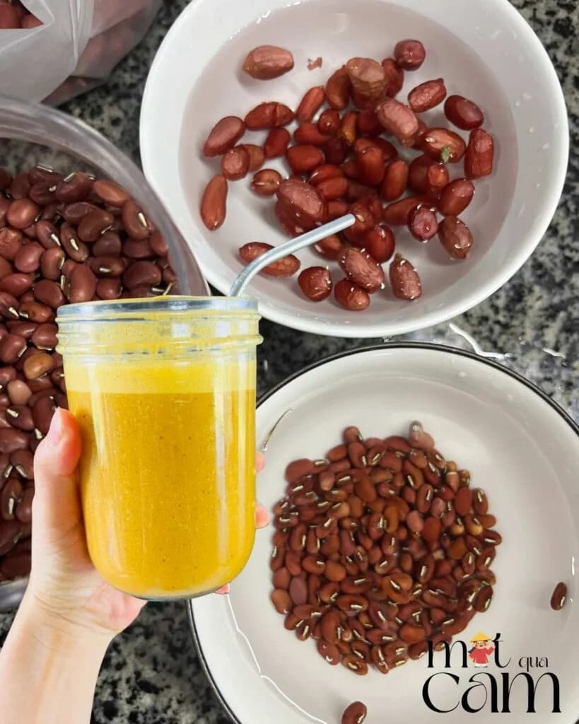 Tay cầm hũ sữa hạt màu vàng, phía sau là các bát lạc và đậu đỏ đã ngâm nước
